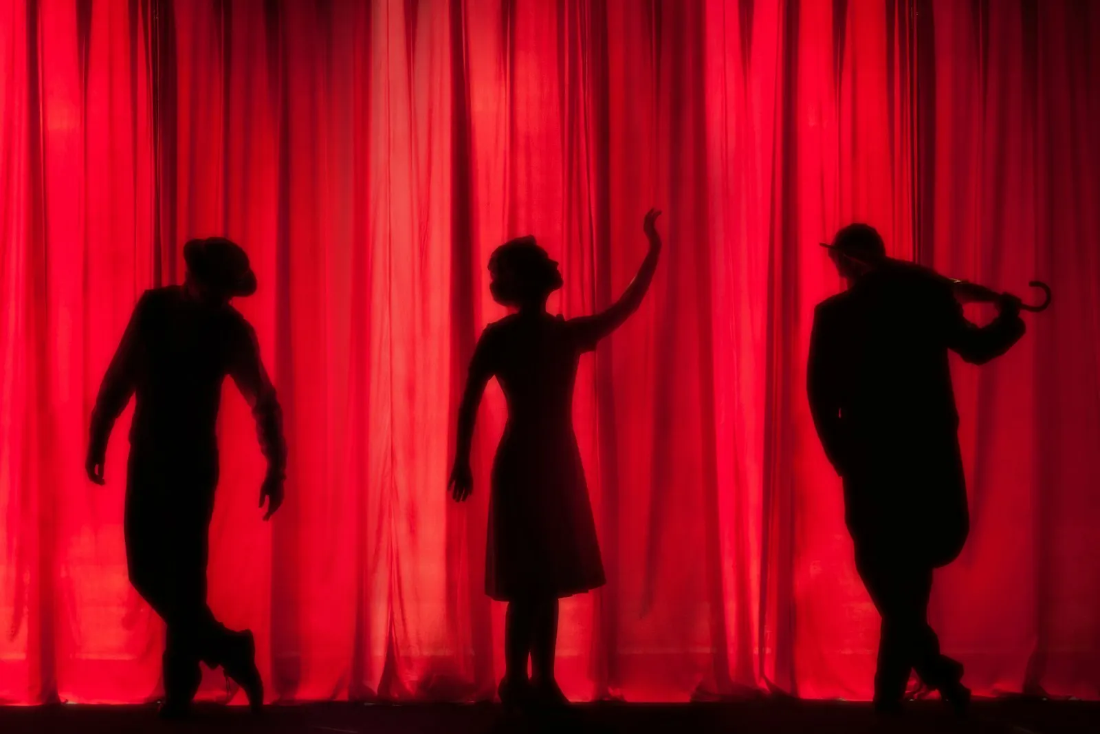 Performers silhouetted against red stage curtains