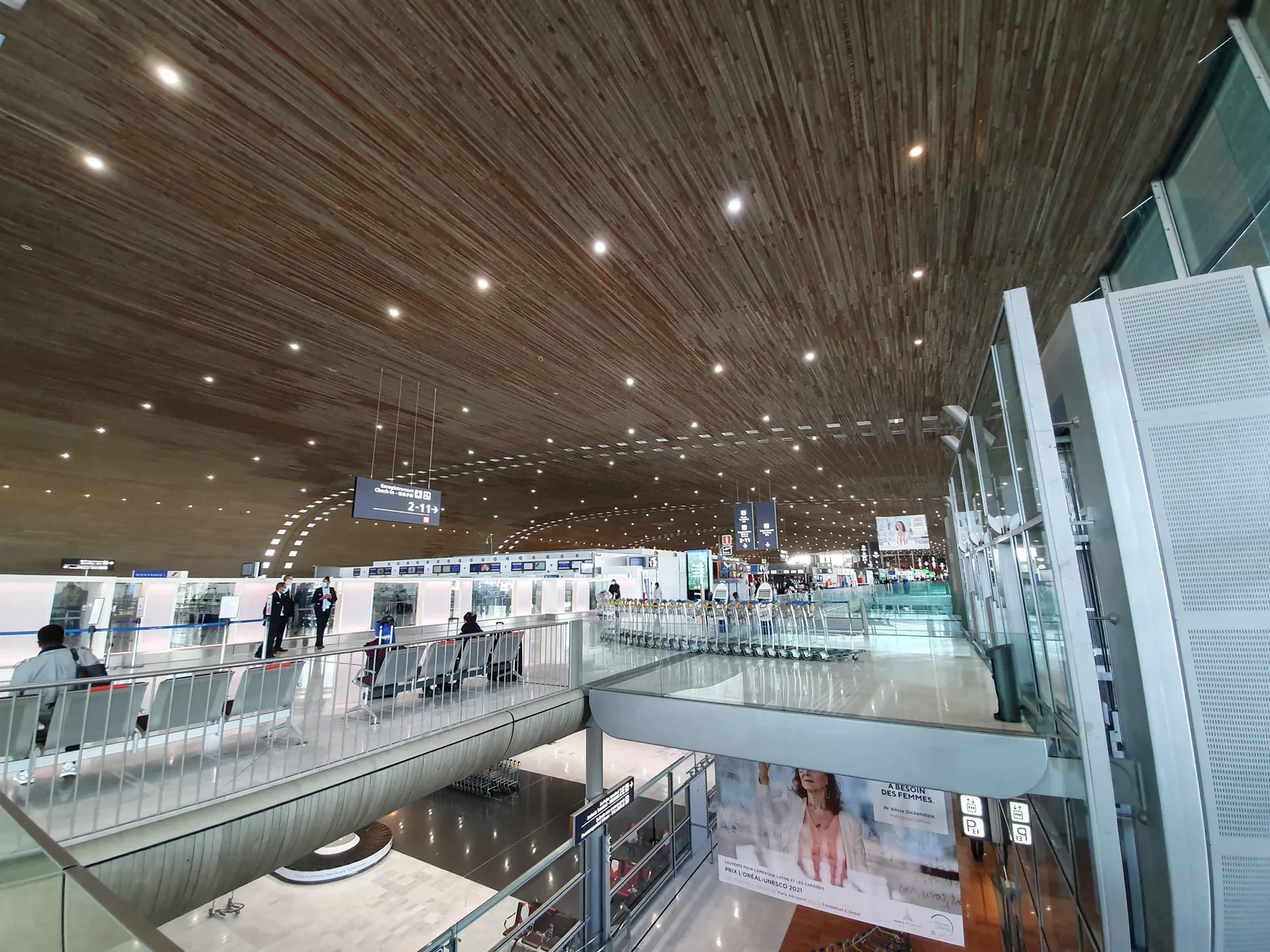Paris–Charles-de-Gaulle Terminal 2E iç mekânı; bankolar, bagaj arabaları ve kavisli ahşap tavan, Ekim 2021